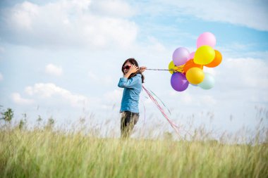 Yeşil çayır bulutu üzerinde koşan balonları tutan bir kadın. Mavi gökyüzü. Mutluluk dolu ve rahatlatıcı. Hava balonları tutan eller doğum günü partisinde oynar Mutlu zamanlar yaz güneşi açık havada