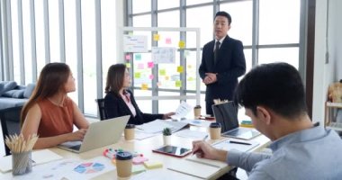 Mutlu iş adamları toplantı odasında grafik çizelgesi yatırımıyla ve iş verileriyle tanışıyor. Bir grup iş adamı konferans odasında toplanıyor. Asyalı iş adamı konuşması, mevcut takım çalışması ortaklığı