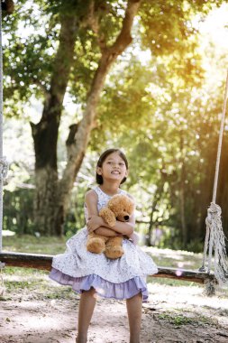 Yeşil Park 'ta oyuncak ayıya sarılırken mutlu çocuk. Oyuncak ayı, küçük çocuklar için en iyi arkadaş tatlı kız. Otizm mutlu bir şekilde oyun bahçesinde birlikte oynayarak mutlu bir aile sevgisi ve sıcacık kucaklaşmayı hisseder.