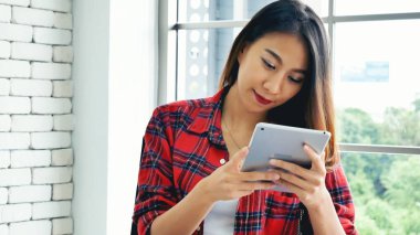 İnternetten dijital tablet alışverişi yapan Asyalı bir kadın arıyor, mesaj yolluyor, internet teknolojisi yaşam tarzında gülümsüyor. Asyalı kadın akıllı tablete dokunuyor mobil uygulama ev ofisini kullanarak ellere odaklanıyor.