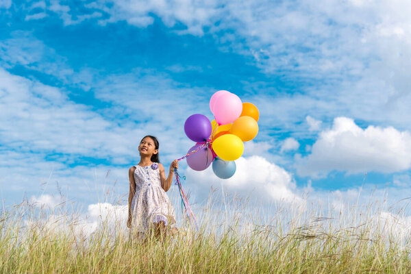 Cheerful cute girl holding balloons running on green meadow white cloud and blue sky with happiness. Hands holding vibrant air balloons play on birthday party happy times summer on sunlight outdoor