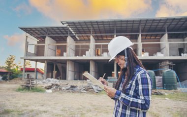 İnşaat mühendisi kadın işçi sanayisinde ekose gömlekli, beyaz kasketli, inşaat işçisi. Mimari mühendis kadın memur emlak projesine bakıyor.