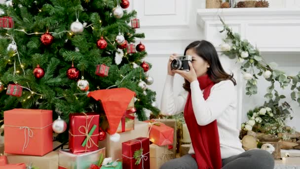 カメラを使用してアジアの女性は居心地の良いリビングルームにクリスマスツリークリスマスプレゼントボックスを撮影します 女性の写真家は 休日の冬の季節のお祝いにバブルボールクリスマスツリーを飾る写真クリスマスを撮る — ストック動画