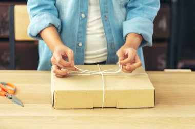 Kadın paket kutusunu masaya koydu. Müşteriye mal teslimatını kontrol ediyor. Asyalı bir kadın ofis masasında küçük bir iş kuruyor. Girişimci Asyalı kadın teslimat için ürün topluyor