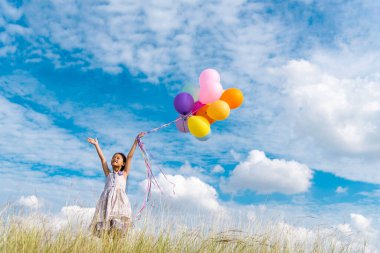 Yeşil çayır üzerinde koşan balonlar tutan neşeli şirin kız beyaz bulut ve mutlulukla mavi gökyüzü. Hava balonları tutan eller doğum günü partisinde oynar. Mutlu zamanlar yaz mevsimi açık havada.