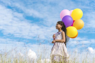 Yeşil çayır üzerinde koşan balonlar tutan neşeli şirin kız beyaz bulut ve mutlulukla mavi gökyüzü. Hava balonları tutan eller doğum günü partisinde oynar. Mutlu zamanlar yaz mevsimi açık havada.