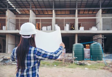 İnşaat mühendisi kadın işçi sanayisinde ekose gömlekli, beyaz kasketli, inşaat işçisi. Mimari mühendis kadın memur emlak projesine bakıyor.