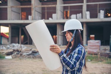 İnşaat mühendisi kadın işçi sanayisinde ekose gömlekli, beyaz kasketli, inşaat işçisi. Mimari mühendis kadın memur emlak projesine bakıyor.