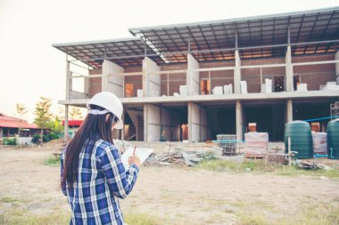 Kadın inşaat mühendisi not yazarken ekose gömlekli beyaz kasketli şantiye işçisi. Mimari Kadın Tasarımı Mühendis İnşaat Kurumu Gayrimenkul
