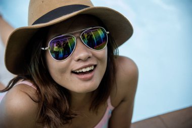 Asyalı kadınlar yaz zamanı mavi gölde yüzerler. Mutlu kadınlar bikini mayo giyer, açık havuzda hasır şapka takar. Genç güzel gezgin havuz kenarı spa tatil köyü yaz konsepti