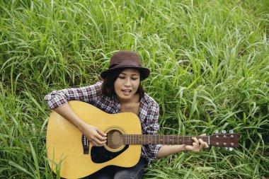 Yeşil parkta akustik gitar çalan genç kadınlar. Evde akustik gitar enstrümanı çalan bir kadın, güzel doğada genç Asyalı müzisyen kız yaşam tarzı. Mutlu gitarist