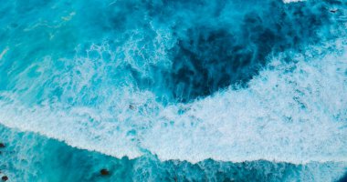 Turkuaz okyanus suyu beyaz dalga deseni derin mavi denize sıçrıyor. Deniz manzaralı karanlık okyanus dalgaları kayalara çarpıyor. Yazın açık deniz sahillerinde tropik deniz plajı. Su yüzeyindeki mavi dalga deseni