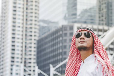 İslami Arap adam tesettür ve Müslüman resmi elbise giyer. Çok kültürlü iş adamları gülümser. Modern şehir manzarasında kameraya bakarlar..