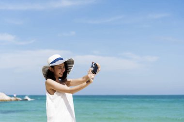 Yaz aylarında mavi gökyüzünde dijital kamera kullanan bir kadın gezgin fotoğraf çekiyor. Asyalı Fotoğrafçı Kadınlar yaz aylarında plajda rahatlar. Mutlu gülümseyen kadın fotoğraf çekerken okyanus adasının tadını çıkar