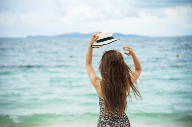 Yazlık kumsalda oturan kadınlar yaz elbisesi ve hasır şapka giyerler. Beyaz kum mavisi deniz. Tropik plaj hayatı yaşayan bir kadın. Gezgin kadın plaj özgürlüğü rahatlığı doğanın tadını çıkar denize bak