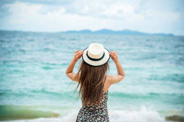 Yazlık kumsalda oturan kadınlar yaz elbisesi ve hasır şapka giyerler. Beyaz kum mavisi deniz. Tropik plaj hayatı yaşayan bir kadın. Gezgin kadın plaj özgürlüğü rahatlığı doğanın tadını çıkar denize bak