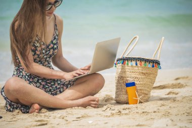 Kadın gezginler yaz aylarında mavi gökyüzünde dizüstü bilgisayar kullanırlar. Kapalı kadın elleri gündelik elbiseler rahat bir şekilde tropik plaj adasında oturuyor. Dizüstü bilgisayar yazan bir kadın tatil tatili iş seyahatinde serbest çalışıyor.