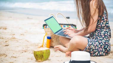 Kadın gezginler yaz aylarında mavi gökyüzünde dizüstü bilgisayar kullanırlar. Kapalı kadın elleri gündelik elbiseler rahat bir şekilde tropik plaj adasında oturuyor. Dizüstü bilgisayar yazan bir kadın tatil tatili iş seyahatinde serbest çalışıyor.