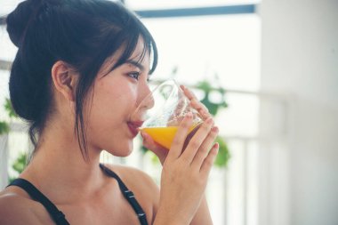 Asyalı kadınlar güler, kameralı sağlık hizmetleri yaşam tarzına bakarlar. Kadın elleri soğuk portakal suyu tutuyor taze meyve suyu içiyor. Güzel bir kadın kokteyl şişesinden portakal suyu dolduruyor.