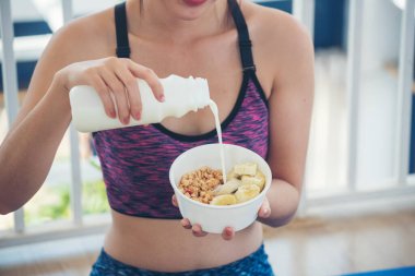 Süt organik besin maddeleriyle yulaf ezmesi yiyen Asyalı kadınlar. Kadınlar ellerinde kaşık ve kase ile sağlıklı süt ürünleri mısır gevreği, meyve ve muz tutuyorlar. Evde sağlıklı beslenme tarzı