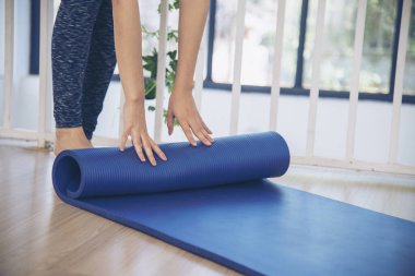 Kadın elleri yoga antrenman odasında jimnastik zemininde yoga minderini sardı. Egzersiz yapan kadın, köpüklü yoga paspası saran elleri kapıyor. Kadın yalınayak evde spor yapıyor sağlıklı yaşam tarzı konsepti