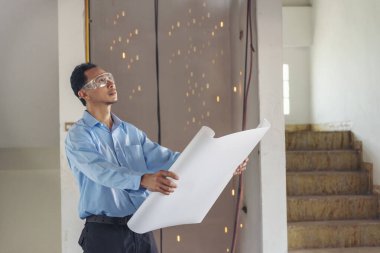 Mimarcı mühendis inşaat işçisi planlara bakıyor. İnşaat mühendisi, mavi gömlek, beyaz şapka şantiyesi giyiyor. Sanayi işçisi gayrimenkul kavramı