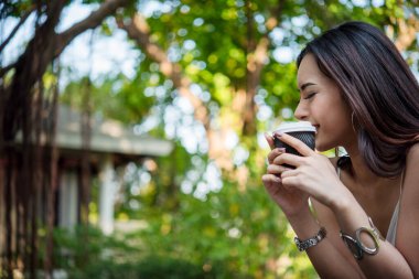 Yeşil Park 'ta kahve içen bir kadın elinde sıcak tek kullanımlık bardak tutuyor. Happy rahatla güzel Asyalı kadın gülümseyen yüz açık hava bahçesinde duruyor. Genç kadınlar doğanın tadını çıkarıyorlar Özgürlük yaşam tarzı.