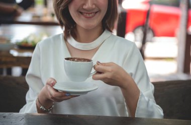 Asyalı kadın kafeterya bahçesinde kahve bardağı tutarken sade kahve içer. Genç kadın gülümsüyor, aşk gülüyor, kahve içiyor. Kafede siyah çay fincanı içen aktif bir kadın elinde taze fincanla. Kadın yaşam tarzı kafe