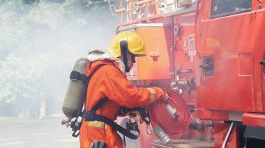 İtfaiyeci itfaiye aracında ekipman hazırla. Yangın söndürücüyle el ele tutuşan bir adam. İtfaiyeci yangın hortumu, tüp, kimyasal su köpüğü polis kurtarma eğitimi kullanıyor.
