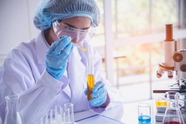 Kimyasal test sarı cam tüpü elinde tutan bilim kadını bilim laboratuvarını test ediyor. Laboratuvar teknisyeni cam tüp idrar örneğine altın sıvısı bırakıyor. Tıbbi kimyada çalışan Asyalı kadın bilim adamı