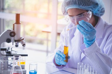 Kimyasal test sarı cam tüpü elinde tutan bilim kadını bilim laboratuvarını test ediyor. Laboratuvar teknisyeni cam tüp idrar örneğine altın sıvısı bırakıyor. Tıbbi kimyada çalışan Asyalı kadın bilim adamı