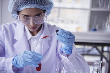 Kimyasal test tüpü tutan bilim laboratuarındaki bilim kadını. Cam tüp tanısı için kırmızı damlayı tutan laboratuvar teknisyeni kan örneği. Tıbbi kimya testinde çalışan Asyalı kadın bilim adamı