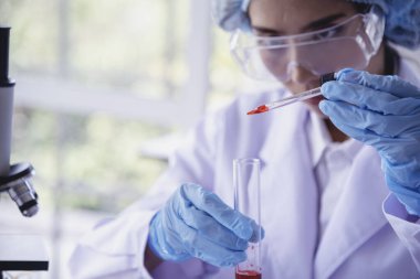 Kimyasal test tüpü tutan bilim laboratuarındaki bilim kadını. Cam tüp tanısı için kırmızı damlayı tutan laboratuvar teknisyeni kan örneği. Tıbbi kimya testinde çalışan Asyalı kadın bilim adamı