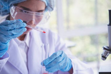 Kimyasal test tüpü tutan bilim laboratuarındaki bilim kadını. Cam tüp tanısı için kırmızı damlayı tutan laboratuvar teknisyeni kan örneği. Tıbbi kimya testinde çalışan Asyalı kadın bilim adamı