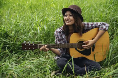 Yeşil parkta akustik gitar çalan genç kadınlar. Evde akustik gitar enstrümanı çalan bir kadın, güzel doğada genç Asyalı müzisyen kız yaşam tarzı. Mutlu gitarist