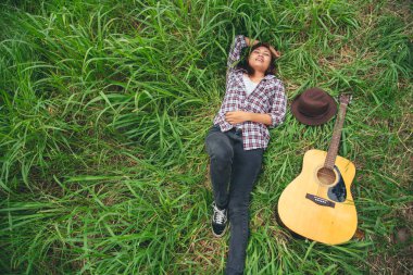 Yeşil parkta akustik gitar çalan genç kadınlar. Evde akustik gitar enstrümanı çalan bir kadın, güzel doğada genç Asyalı müzisyen kız yaşam tarzı. Mutlu gitarist