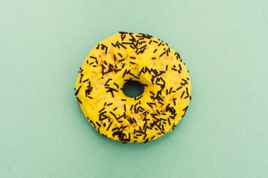 Yeşil arka planda izole edilmiş çikolata parçacıklarıyla süslenmiş sarı çörek. Düz yatıyordu. Üst görünüm