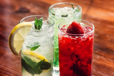 Buzlu yaz ferahlatıcı içecek, çilekli limonata ve uzun bardakta mojito kokteyli, ahşap arka planda.