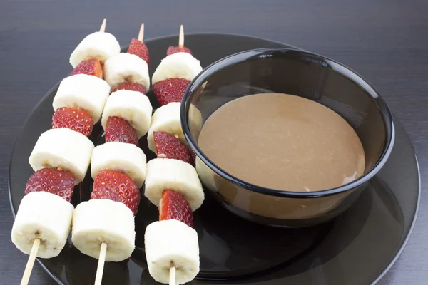 Muz ve çilek eritilmiş çikolata bir kase yanındaki tahta bir sopa üzerinde