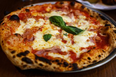 Mozzarella peyniri ve taze fesleğenle kaplı taze pişmiş geleneksel Prosciutto pizzası..