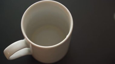 Siyah bir tezgahın üzerine beyaz bir seramik fincana sıcak siyah kahve dökülüyor.