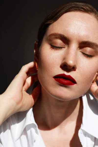 Verticale close-up van mooie vrouw met rode lippen in wit shirt, poserend over donkere achtergrond. — Stockfoto
