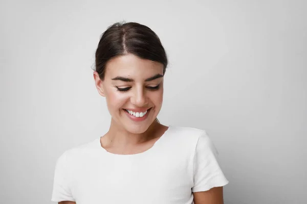 Щаслива молода жінка посміхається в білій футболці, дивлячись вниз. Простір для тексту . — стокове фото