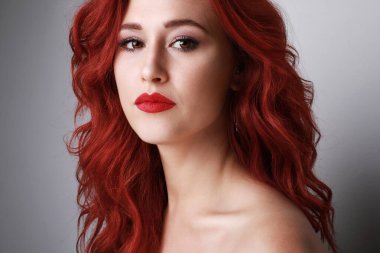 Beyaz duvarın üzerinde poz veren güzel, uzun kızıl saçlı genç bir kadın resmi..