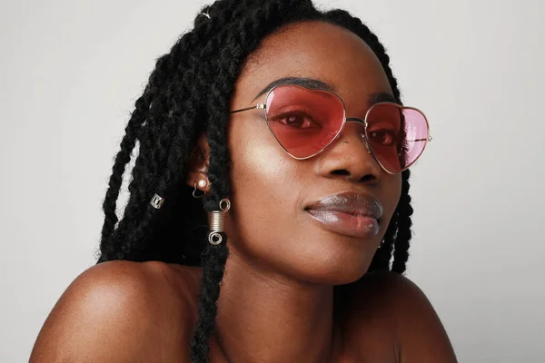 Fiatal fekete nő copfos rózsaszín napszemüveg, pózol a fehér falon. — Stock Fotó
