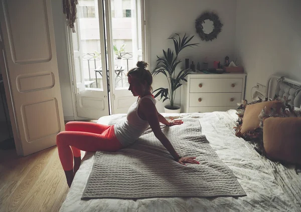 Mulher loira está sentada na cama. A menina está fazendo ioga em casa. Espaço para texto. — Fotografia de Stock