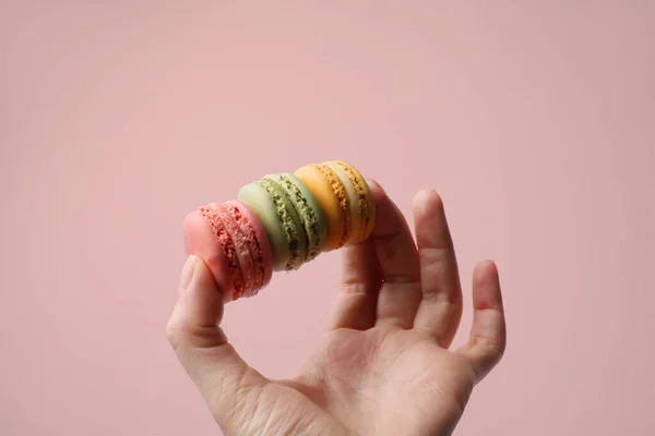 Mano humana sosteniendo macarrones deliciosos crujientes en la pared de fondo rosa. —  Fotos de Stock