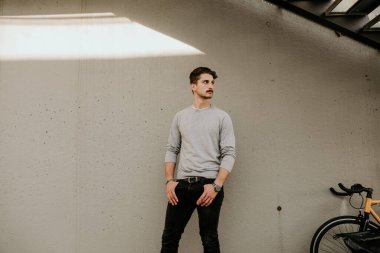 Gri duvarın üzerinde bisikletle poz veren gündelik elbiseli genç adam. Açık hava..