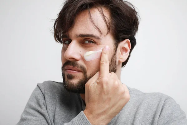 Homem barbudo aplicando hidratar o rosto. A arrumar. Isolado na parede branca. — Fotografia de Stock