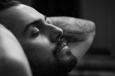 Sakallı adam kapalı gözlerle poz veriyor. Siyah ve beyaz resim.